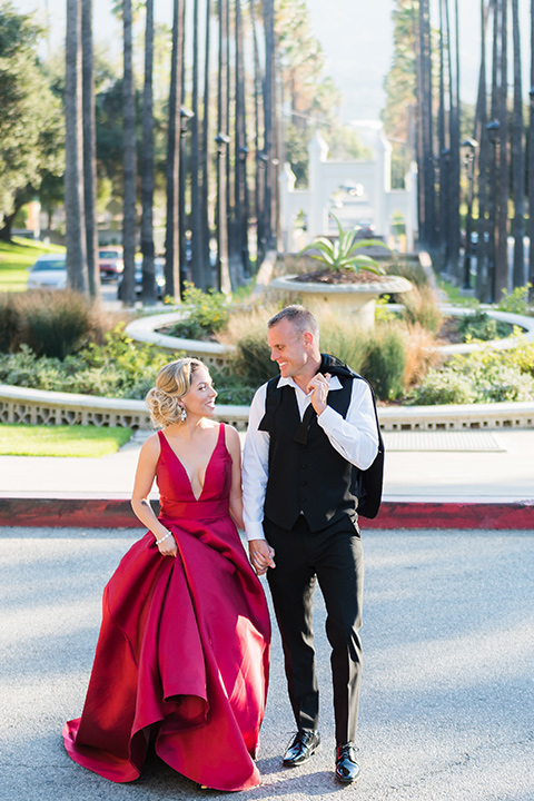 bride in a red evening gown with a plunging neckline and hair in a bun, groom in a black velvet tuxedo and black bow tie