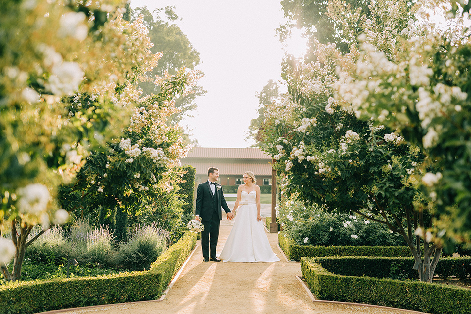  bride in a white strapless ballgown with her hair in a bun, groom in a black tuxedo with a black bow tie 