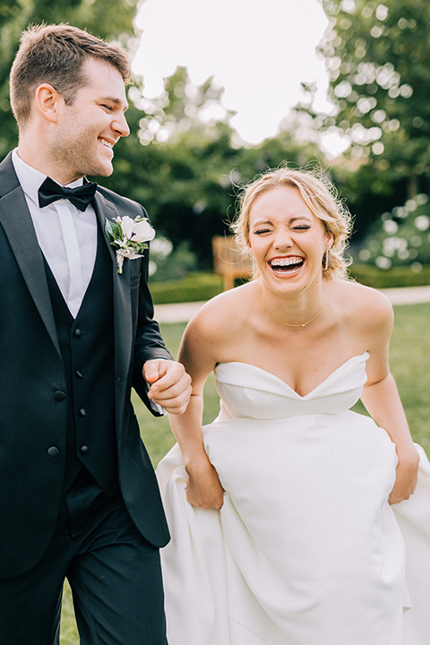  bride in a white strapless ballgown with her hair in a bun, groom in a black tuxedo with a black bow tie 