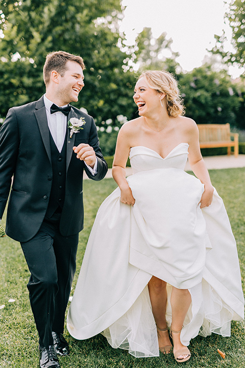 bride and groom running, bride in a white strapless ballgown with a bow detail and hair in a bun, groom in a black tuxedo with a black bow tie