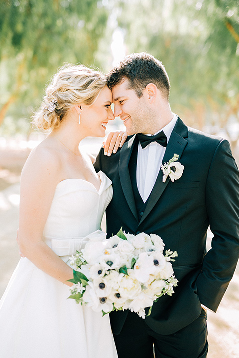 bride and groom touching heads, bride in a white strapless ballgown with a bow detail and hair in a bun, groom in a black tuxedo with a black bow tie