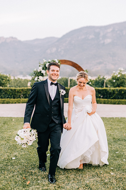  bride in a white strapless ballgown with her hair in a bun, groom in a black tuxedo with a black bow tie 