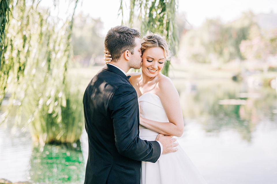  bride in a white strapless ballgown with her hair in a bun, groom in a black tuxedo with a black bow tie 