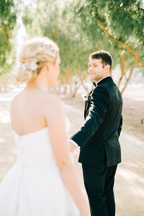  bride in a white strapless ballgown with her hair in a bun, groom in a black tuxedo with a black bow tie 