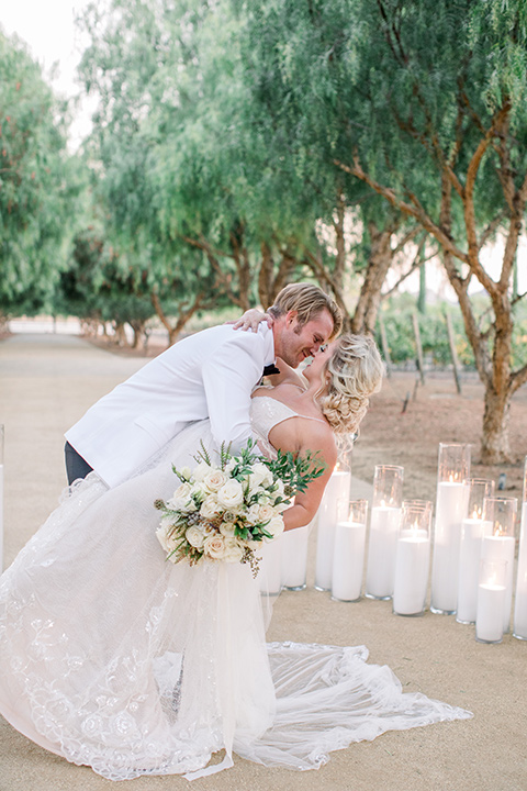 groom dipping bride, bride in a white gown with a plunging neckline and a sheer cape and train and the groom in a white jacket and black pants 