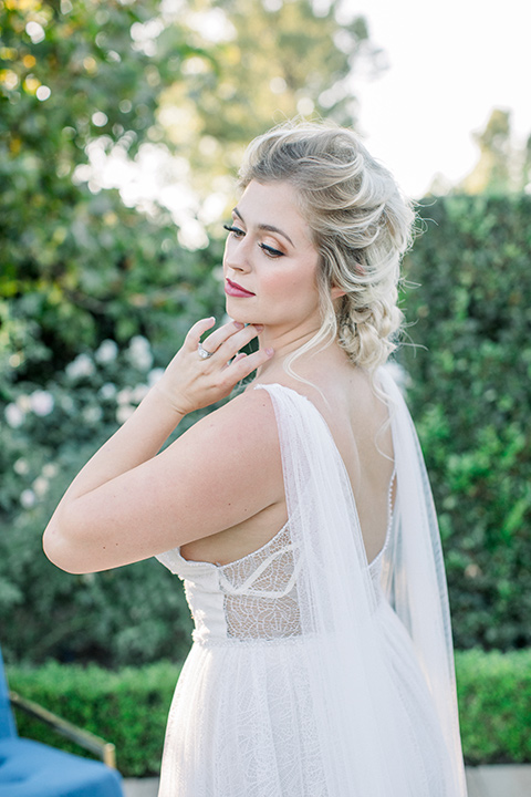  bride in a white gown with a plunging neckline and a sheer cape and train with her hair in a bun 