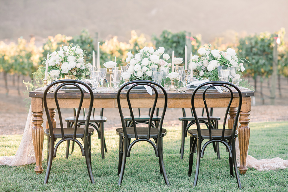 wooden table with white flatware and white florals and black chairs