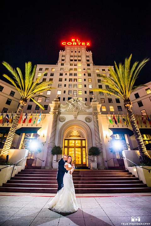 San-Diego-Wedding-bride-and-groom-outside-buiding-at-night-the-bride-is-in-a-white-lace-gown-with-an-off-the-shoulder-neckline-groom-in-a-black-tuxedo-with-a-black-bow-tie