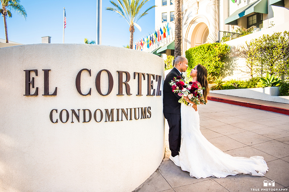 San-Diego-Wedding-bride-and-groom-outside-venue-the-bride-is-in-a-lace-form-fitting-gown-with-an-off-the-shoulder-neckline-groom-is-in-a-black-tuxedo-with-a-black-bow-tie