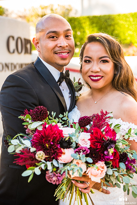 San-Diego-Wedding-bride-and-groom-smiling-at-camera-the-bride-is-in-a-white-lace-gown-with-an-off-the-shoulder-neckline-groom-in-a-black-tuxedo-with-a-black-bow-tie