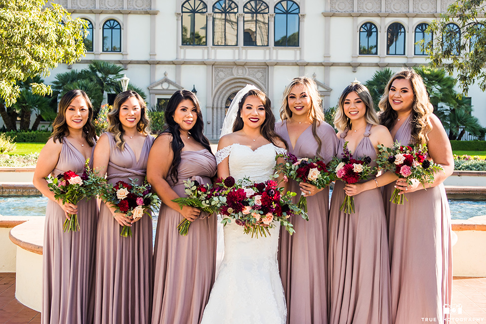 San-Diego-Wedding-bridesmaids-the-bride-is-in-a-lace-form-fitting-gown-with-an-off-the-shoulder-neckline-the-bridesmaids-in-mauve-pink-gowns