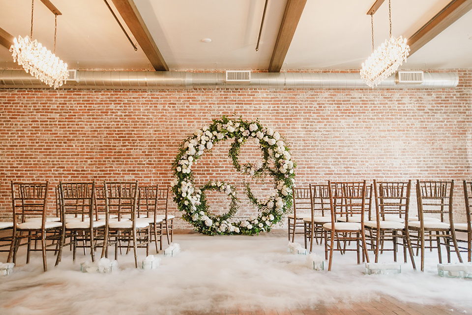 circular floral arch and wooden chairs, with a white faux fur carpet on the ground