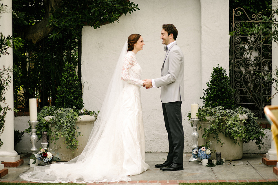 The bride in a white gown with lace long sleeves and a high neckline the groom in a light grey suit with black pants and a grey velvet bow tie