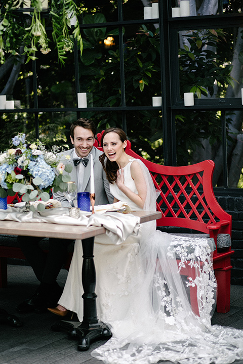 bride in a white lace gown with cap sleeves and a light grey suit coat and black pants with a grey velvet bow tie
