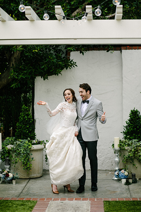 bride in a white lace gown with cap sleeves and a light grey suit coat and black pants with a grey velvet bow tie