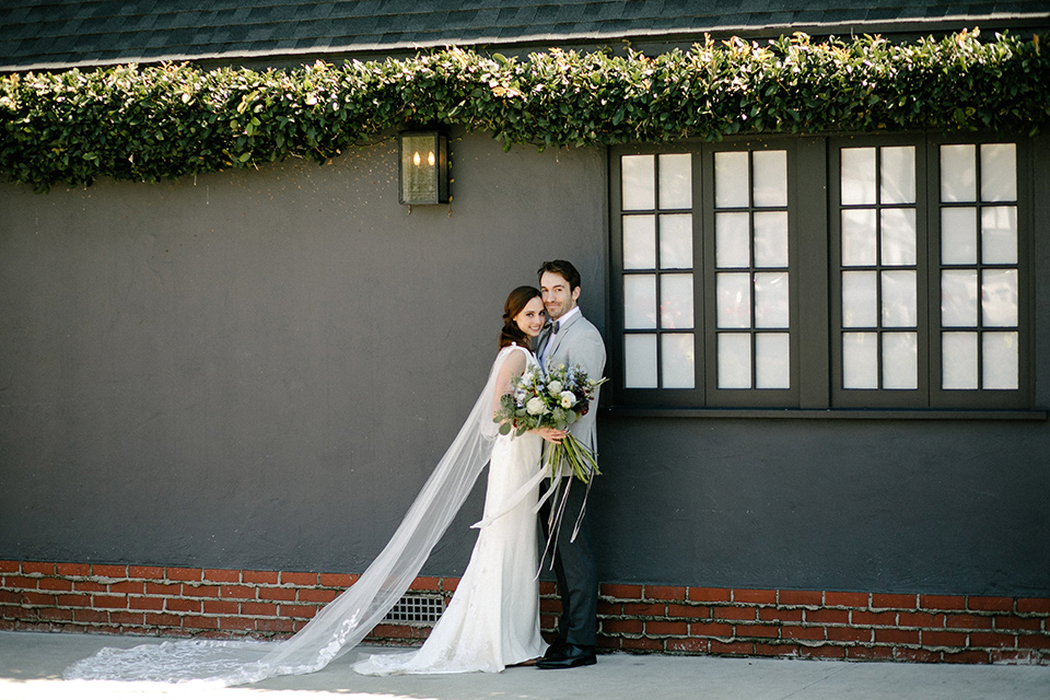 The bride in a white gown with lace long sleeves and a high neckline the groom in a light grey suit with black pants and a grey velvet bow tie