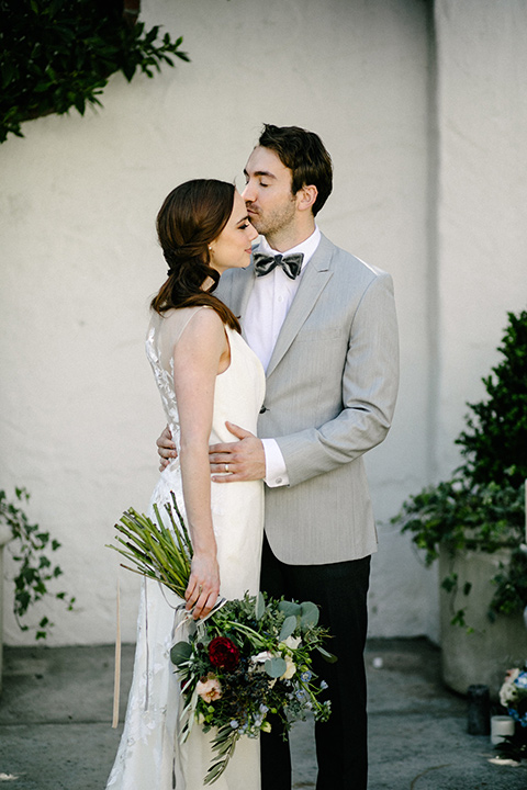 bride in a white flowing gown with cap sleeves and the groom in a grey suit coat with a pair of black pants and a velvet grey bow tie