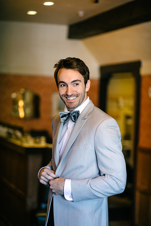groom in a grey suit coat with a pair of black pants and a velvet grey bow tie