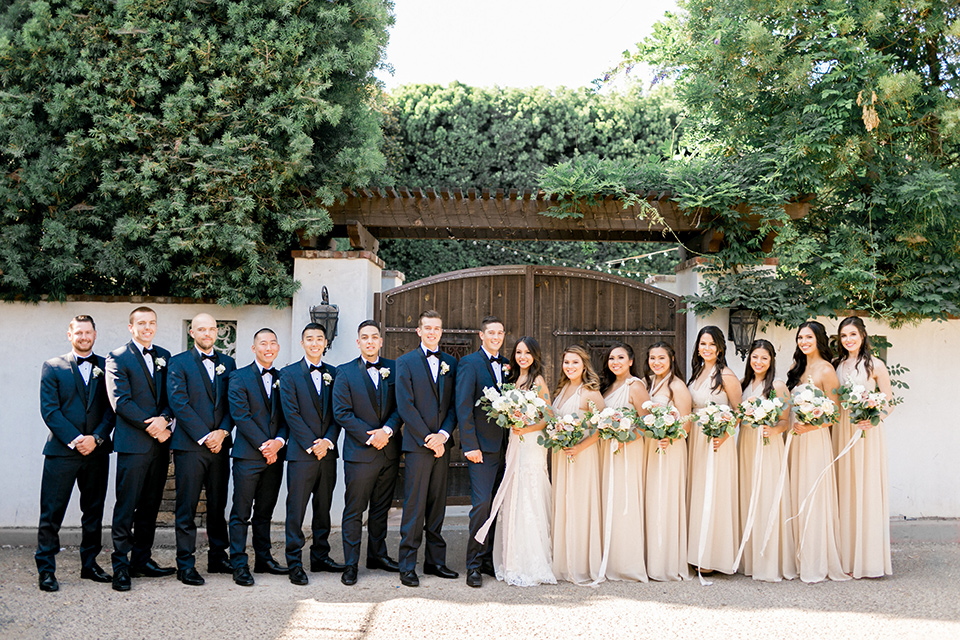 franciscan-gardens-wedding-bridal-party-lined-up-bridesmaids-in-a-light-chamagne-color-groomsmen-in-navy-suits-bride-in-a-white-mermaid-strapless-gown-with-hair-down-and-simple-groom-in-a-navy-shawl-lapel-tuxedo-with-a-black-bow-tie