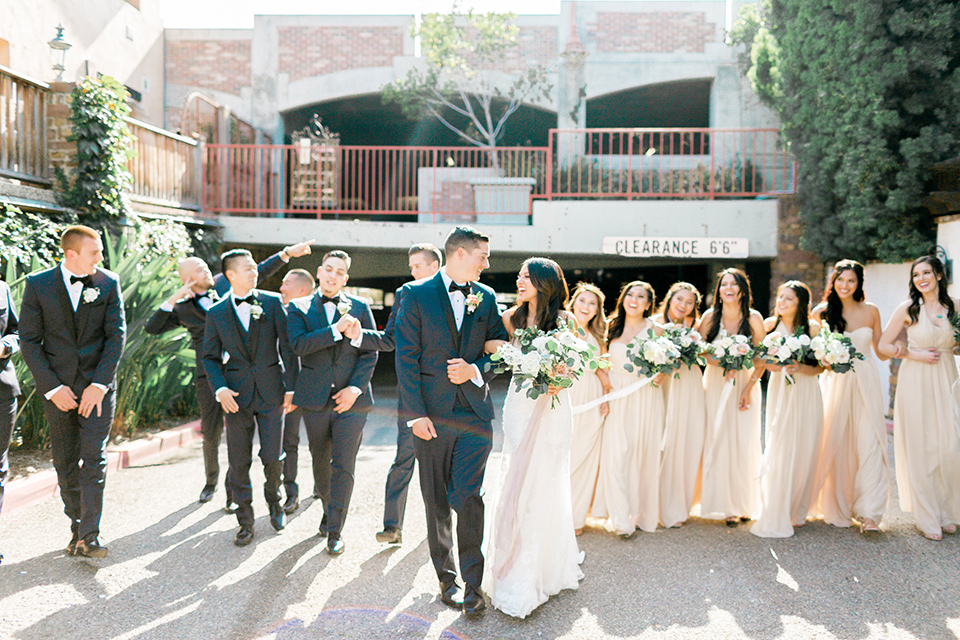 franciscan-gardens-wedding-bridal-party-walking-bridesmaids-in-a-light-chamagne-color-groomsmen-in-navy-suits-bride-in-a-white-mermaid-strapless-gown-with-hair-down-and-simple-groom-in-a-navy-shawl-lapel-tuxedo-with-a-black-bow-tie