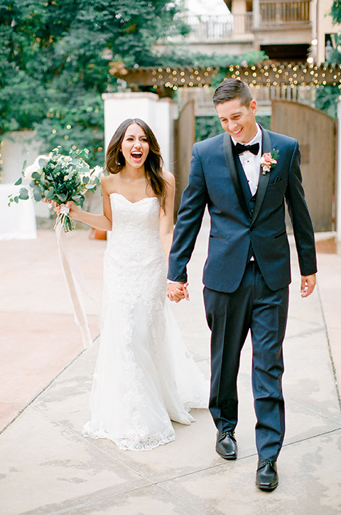 franciscan-gardens-wedding-bride-and-groom-walking-and-smiling-bride-in-a-strapless-form-fitting-white-gown-groom-in-a-navy-shawl-lapel-tuxedo-with-black-accessories