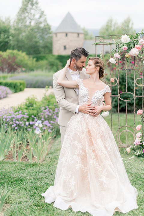 bride in a champagne and blush colored gown with the groom in a tan suit with a champagne bow tie in the garden