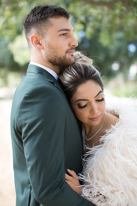 bride in a fur cape and hair in a high bun with her head resting on her groom in a green suit