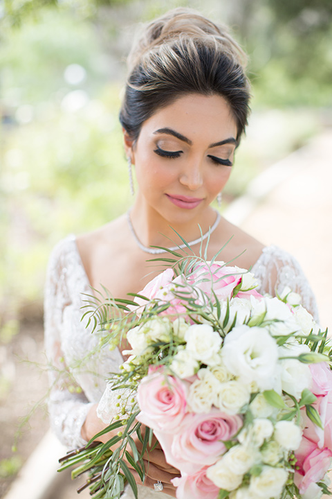 bride in a lace gown with long sleeves and a bouquet of white and pink florals