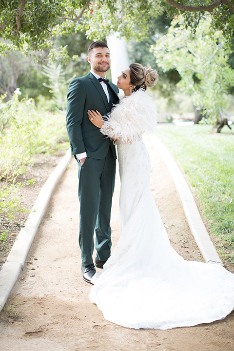 bride in a lace gown with a white fur cape and the groom in a green suit