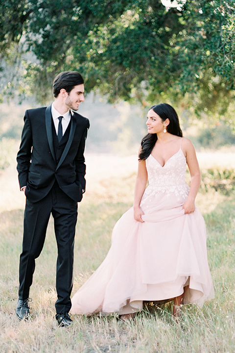 bride in a blush bridal gown with thin straps and a sweetheart neckline and the groom in a black shawl lapel tuxedo with a black long tie