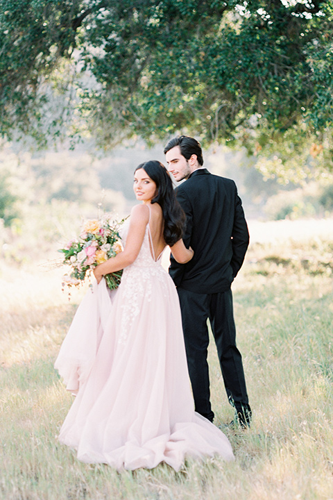 bride in a blush colored gown with thin straps and a sweetheart neckline and the groom in a black shawl lapel tuxedo with a black long tie