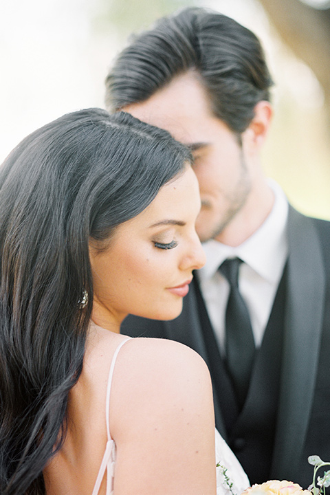 bride in a blush bridal gown with thin straps and a sweetheart neckline and the groom in a black shawl lapel tuxedo with a black long tie