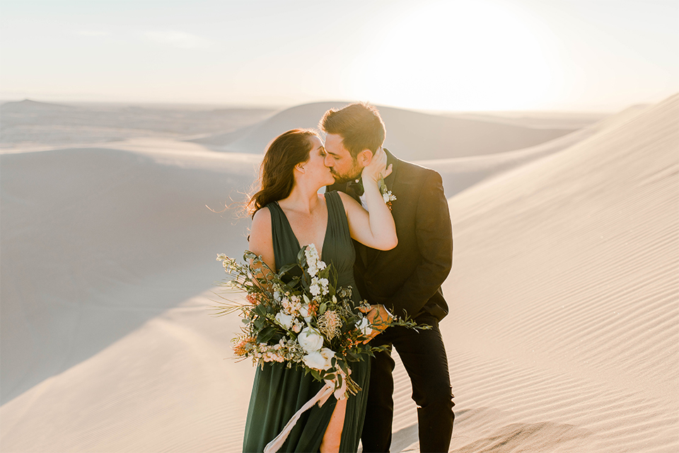 Glamis-Engagement-Shoot-bride-and-groom-holding-hands-bride-in-a-deep-green-flowing-dress-with-a-plunging-neckline-groom-in-a-black-tuxedo-with-navy-blue-velvet-bow-tie