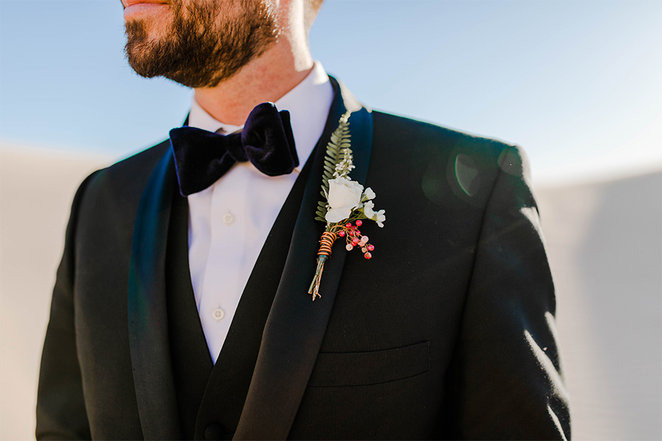 Glamis-Engagement-Shoot-closeup-on-groom-bride-in-a-deep-green-flowing-dress-with-a-plunging-neckline-groom-in-a-black-tuxedo-with-navy-blue-velvet-bow-tie