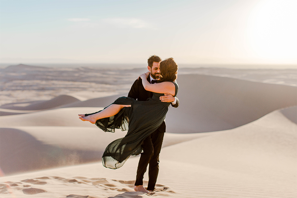 Glamis-Engagement-Shoot-groom-holding-bride-bride-in-a-deep-green-flowing-dress-with-a-plunging-neckline-groom-in-a-black-tuxedo-with-navy-blue-velvet-bow-tie