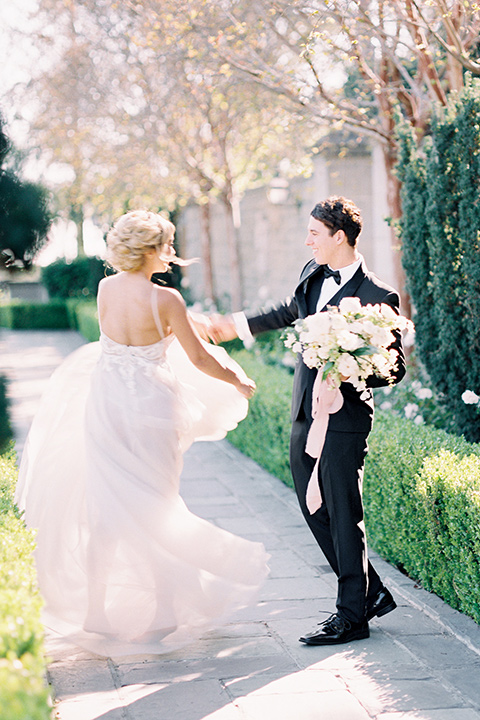 bride wearing a tulle ballgown with thin straps and her hair in a loose braided bun and the groom in a black tuxedo with a black bow tie twirling