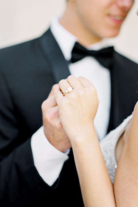  bride wearing a tulle ballgown with thin straps and her hair in a loose braided bun with a peony and rose bouquet and the groom in a black tuxedo and a black bow tie close up and holding hands