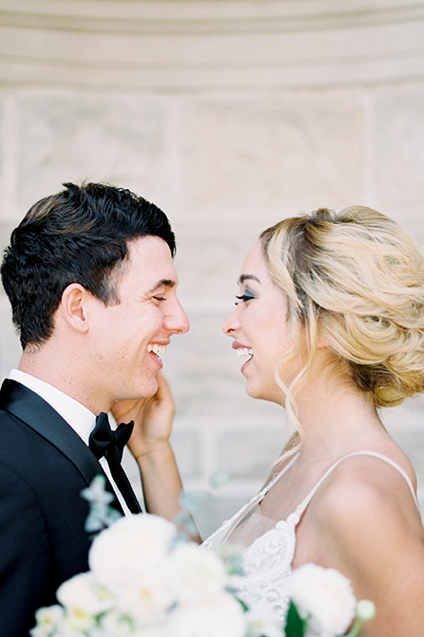 bride wearing a tulle ballgown with thin straps and her hair in a loose braided bun and the groom in a black tuxedo with a black bow tie smiling at each other