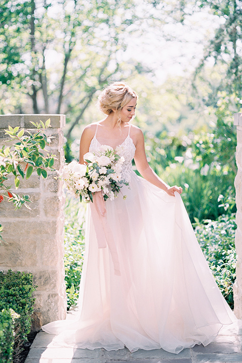  bride wearing a tulle ballgown with thin straps and her hair in a loose braided bun with a peony and rose bouquet