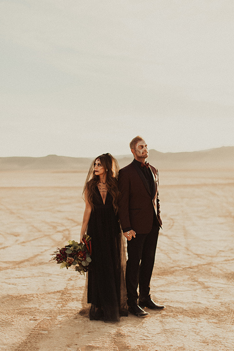 Halloween shoot with the bride in a black and burgundy tulle gown with a black veil and the groom in a burgundy tuxedo with a black trim, a black shirt, and a burgundy bow tie looking in different directions