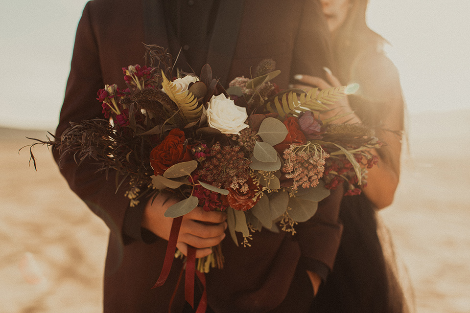 Halloween-Shoot-close-up-on-floral-arrangements and groom in a burgundy tuxedo with a black shirt and burgundy bow tie