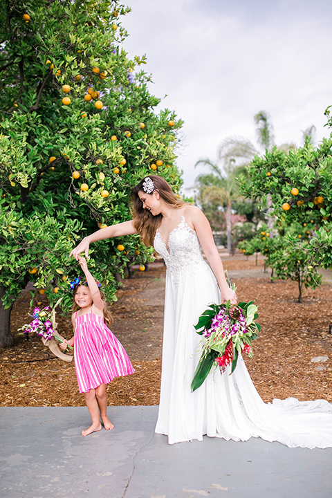 bride holding a tropical floral bouquet in her boho gown and floral headband with flower girl in a pink dress and matching headband