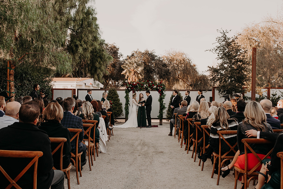 Highway-West-Vacations-bride-and-groom-ceremony-bridesmaids-in-dark-green-dresses-groomsmen-in-black-tuxedos-with-green-velvet-bow-ties-bride-in-a-lace-bohemian-dress-with-sleeves-and-floral-crown-groom-in-a-black-tuxedo