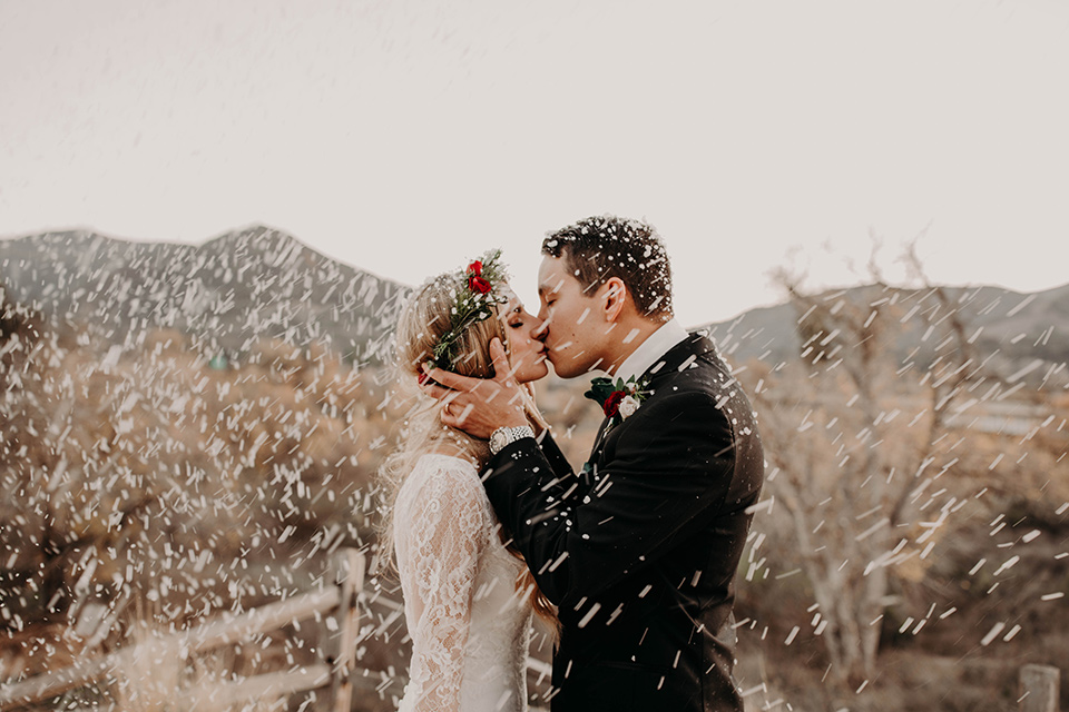 Highway-West-Vacations-bride-and-groom-kissing-in-the-snow-kissing-bride-in-a-lace-bohemian-dress-with-sleeves-and-floral-crown-groom-in-a-black-tuxedo