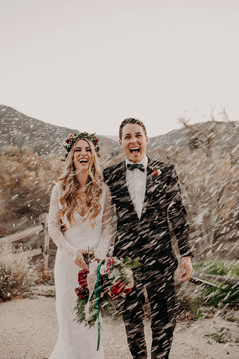 Highway-West-Vacations-bride-and-groom-smiling-in-the-snow-bride-alone-in-a-lace-gown-with-sleeves-and-a-floral-crown-groom-in-a-black-tuxedo-with-a-velvet-bow-tie