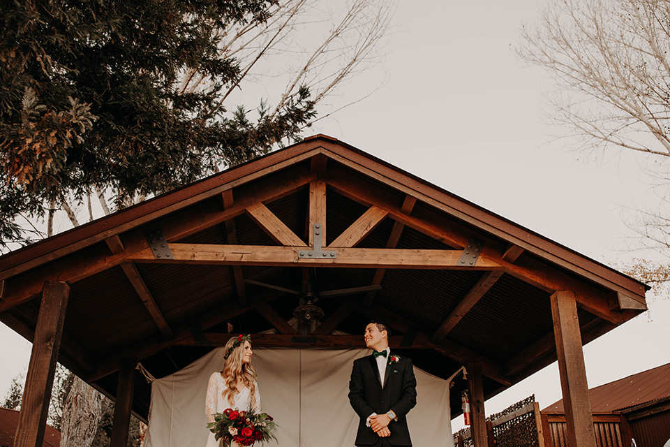 Highway-West-Vacations-bride-and-groom-under-gazebo-bride-in-a-lace-bohemian-dress-with-sleeves-and-floral-crown-groom-in-a-black-tuxedo