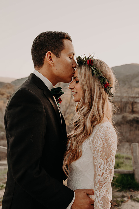 Highway-West-Vacations-groom-kissing-brides-head-groom-alone-in-a-black-tuxedo-with-a-velvet-bow-tie-in-a-white-lace-down-with-sleeves