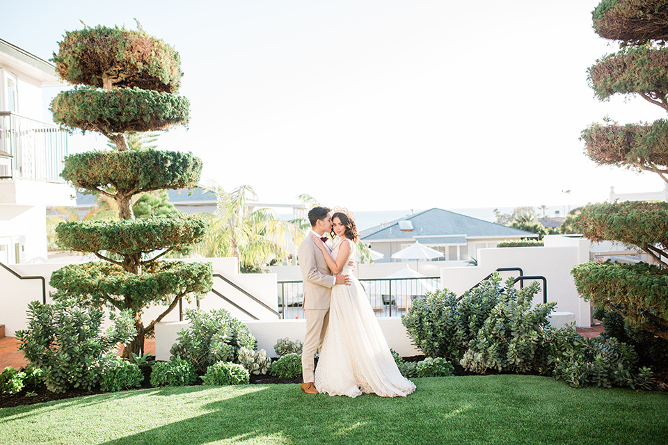  bride in a cream colored bohemian inspired gown with a gold crown, groom in a tan suit with a burgundy velvet bow tie 