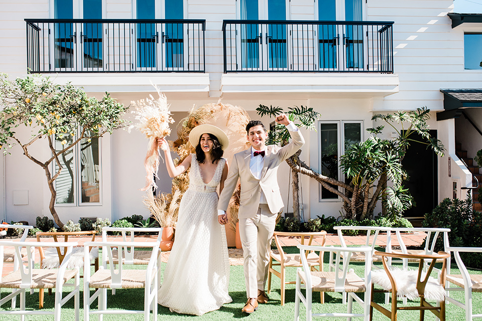  bride in a cream colored bohemian inspired gown with a gold crown, groom in a tan suit with a burgundy velvet bow tie 