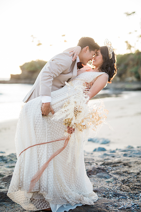  bride in a cream colored bohemian inspired gown with a gold crown, groom in a tan suit with a burgundy velvet bow tie, at the beach 